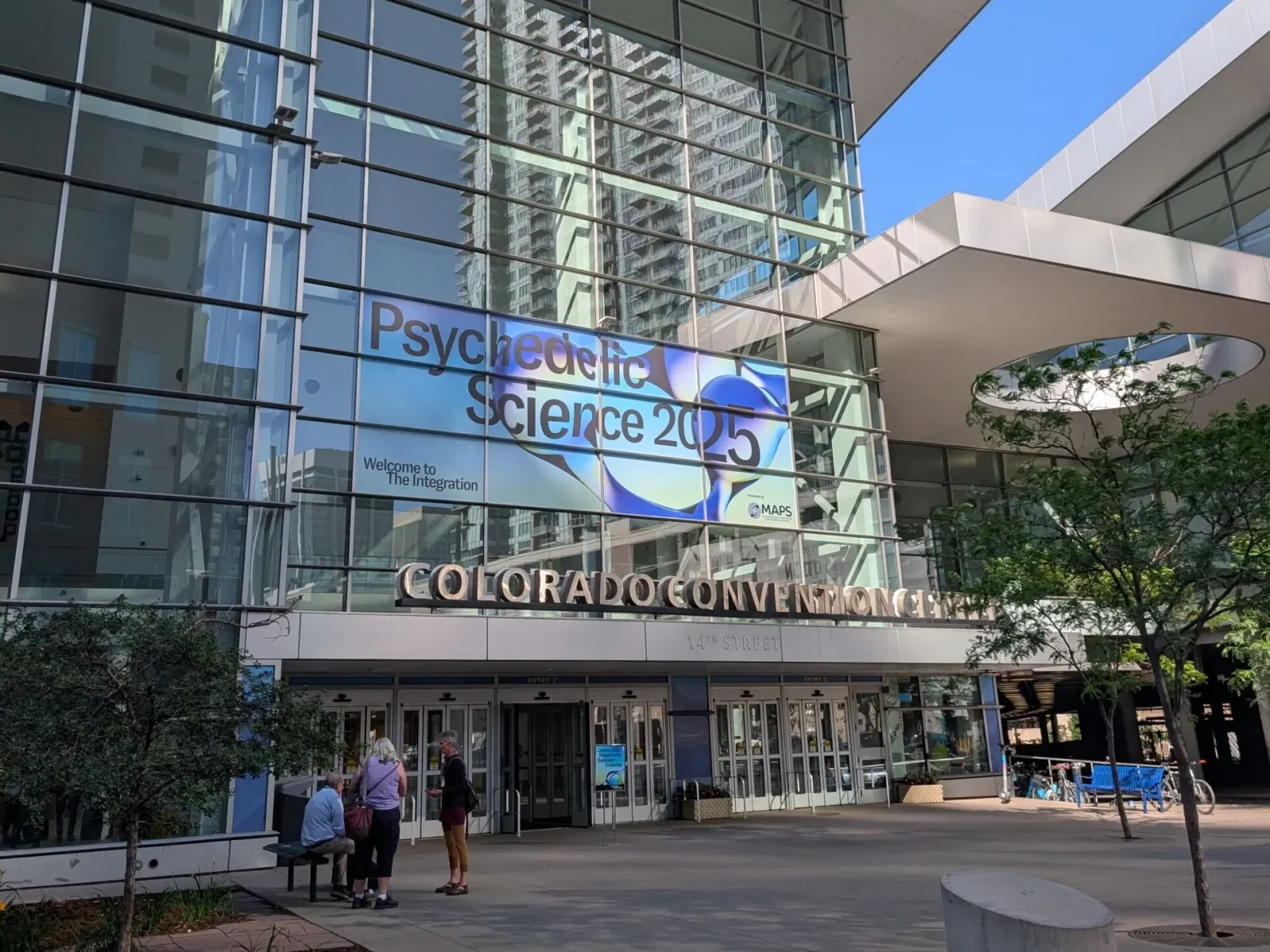 The Colorado Convention Center on 14th Street with the Psychedelic Science 2025 banner across the glass: Welcome to The Integration, presented by MAPS